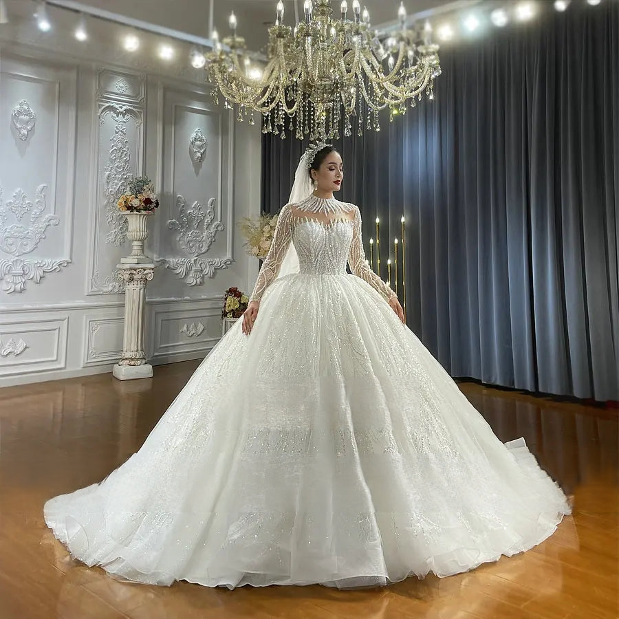 Elegant front perspective of a long-sleeve bridal gown with a beaded bodice and a majestic, sparkling tulle skirt designed for a grand wedding entrance.