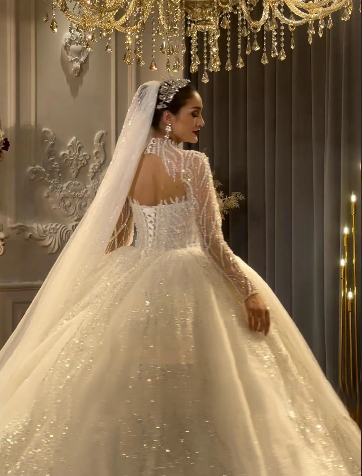 Detailed rear view of a luxury wedding dress highlighting a lace-up corset back, sheer beaded shoulders, and an expansive shimmering cathedral-length train.