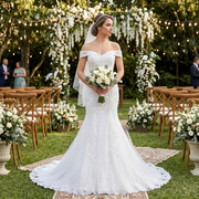 Elegant bride wearing an off-shoulder boat neck mermaid wedding dress, standing in a lush outdoor garden ceremony setting with floral decorations.