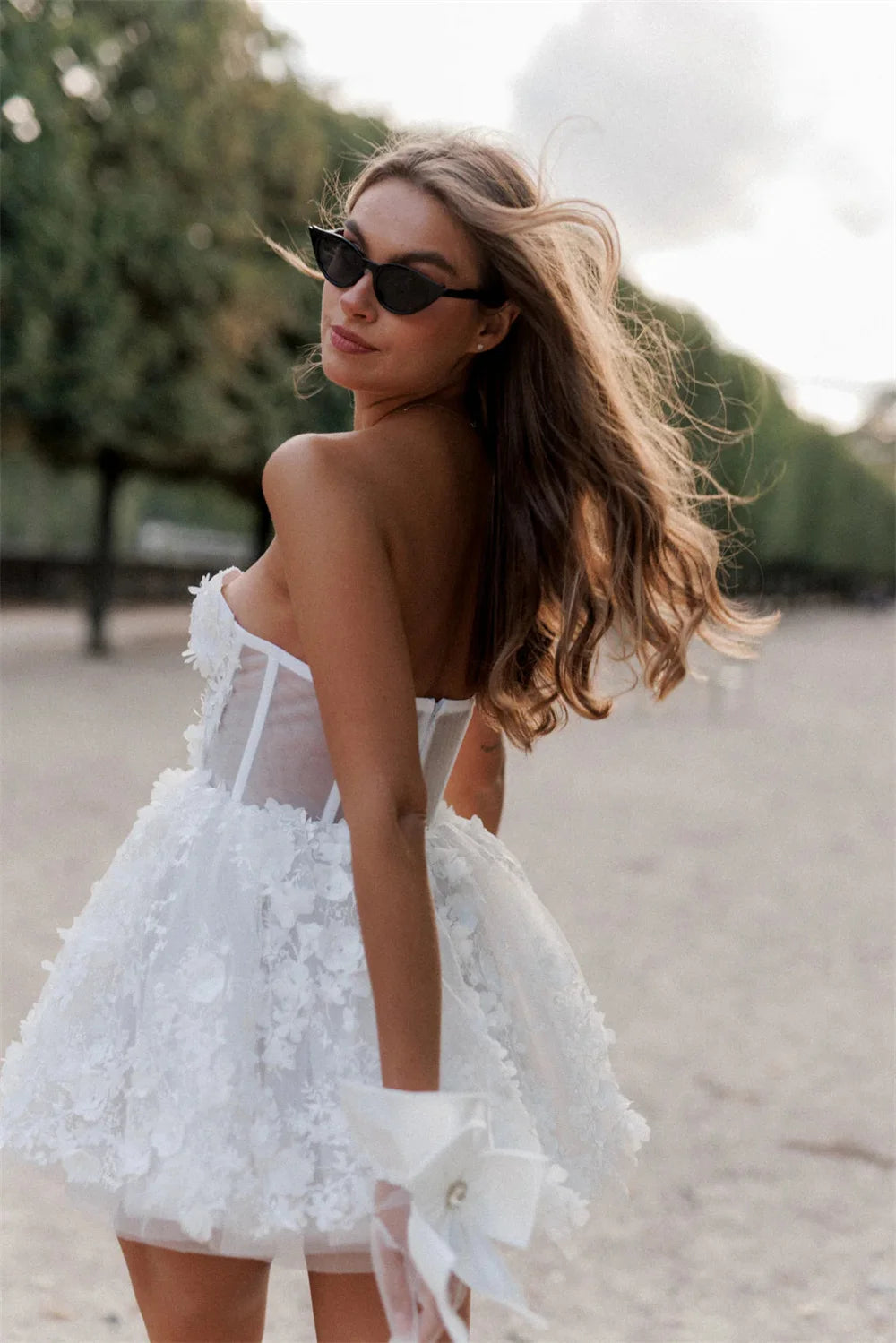 Back view of an elegant white mini party dress featuring delicate floral lace appliques, corset-style bodice, and chic bow wrist gloves.
