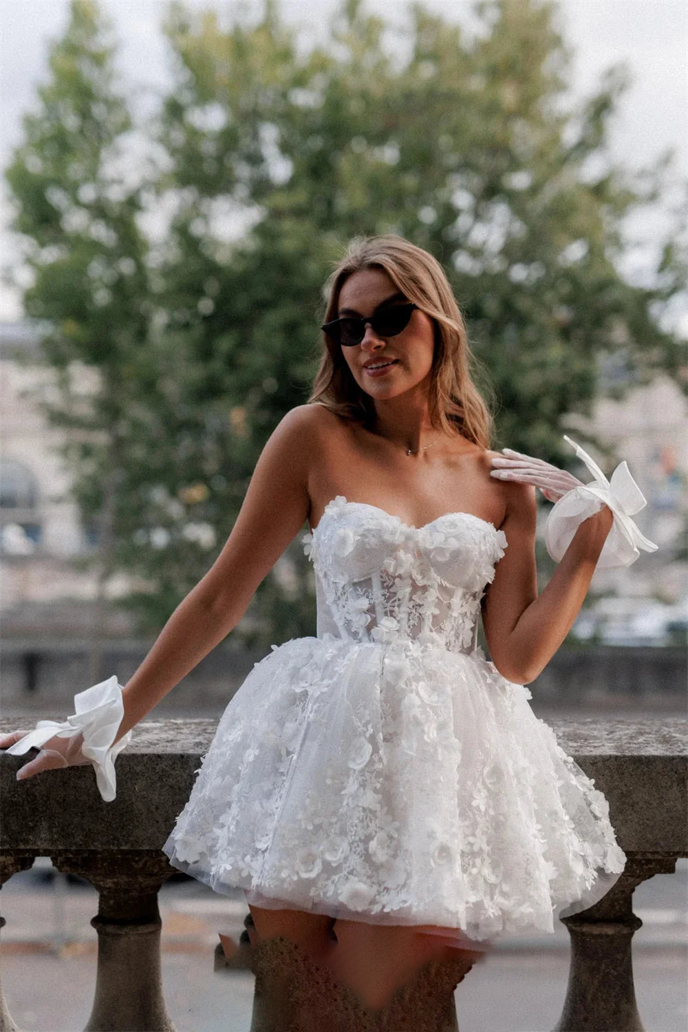 Front-facing editorial shot of a woman in an elegant white mini prom dress with heart-shaped bodice, lace appliques, and stylish wrist gloves.