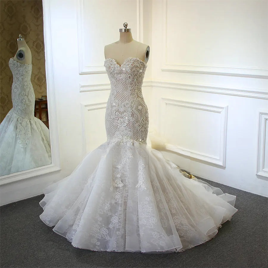 Three-quarter profile view of an elegant champagne mermaid bridal gown on a mannequin, showcasing the strapless sweetheart neckline, full beaded detailing, and voluminous lace-trimmed skirt, with a reflection visible in a mirror.