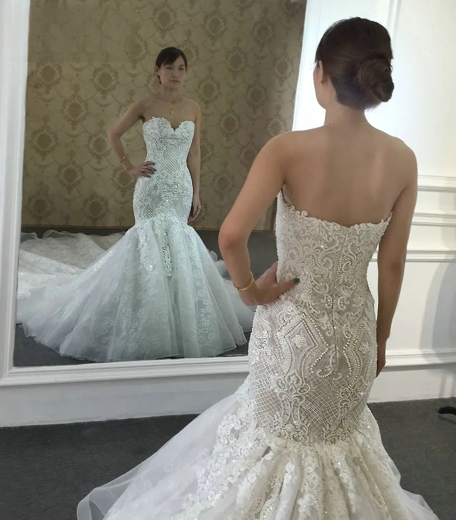 Back view of a bride in a champagne lace mermaid wedding dress looking into a mirror, highlighting the low back and intricate beaded patterns.