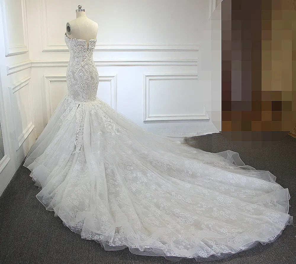 Elegant rear view of a mermaid bridal gown on a mannequin, showcasing the long, spreading cathedral-length lace and tulle train.