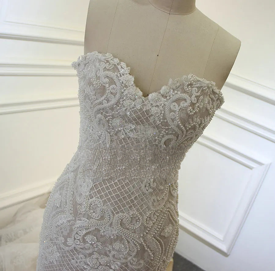 Close-up detail of the sweetheart bodice on a champagne bridal gown, featuring elaborate crystal and pearl beadwork over delicate mesh and lace.