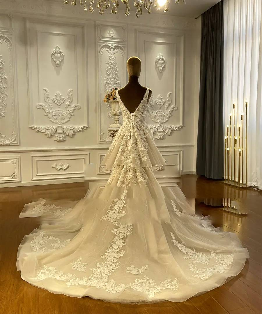 Detailed rear view of an elegant champagne beach bridal gown highlighting the V-back and the expansive train adorned with floral lace appliques.