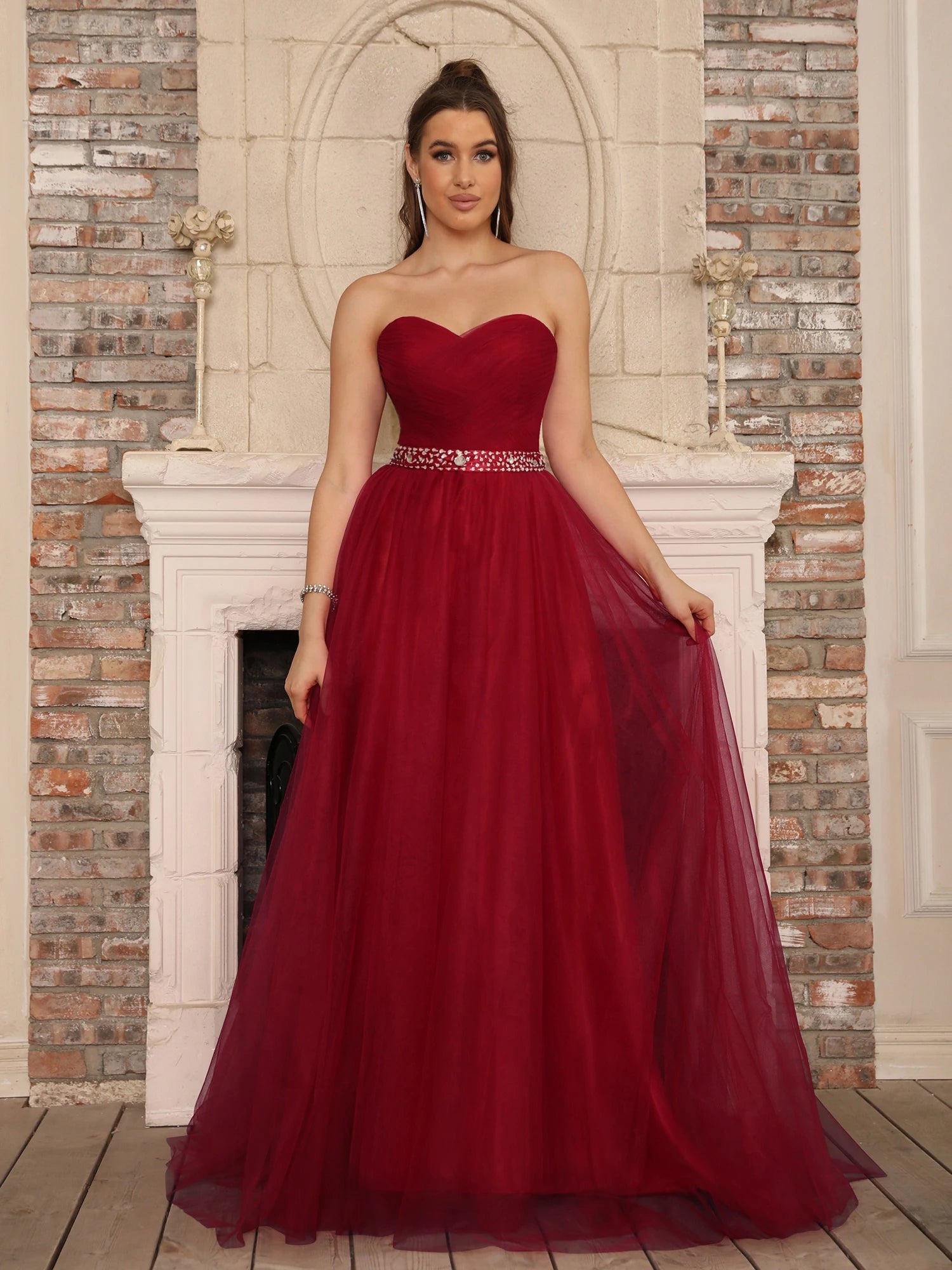 Full-length burgundy sweetheart neck A-line gown with a voluminous tulle skirt and sparkling jeweled belt in a classic indoor setting.