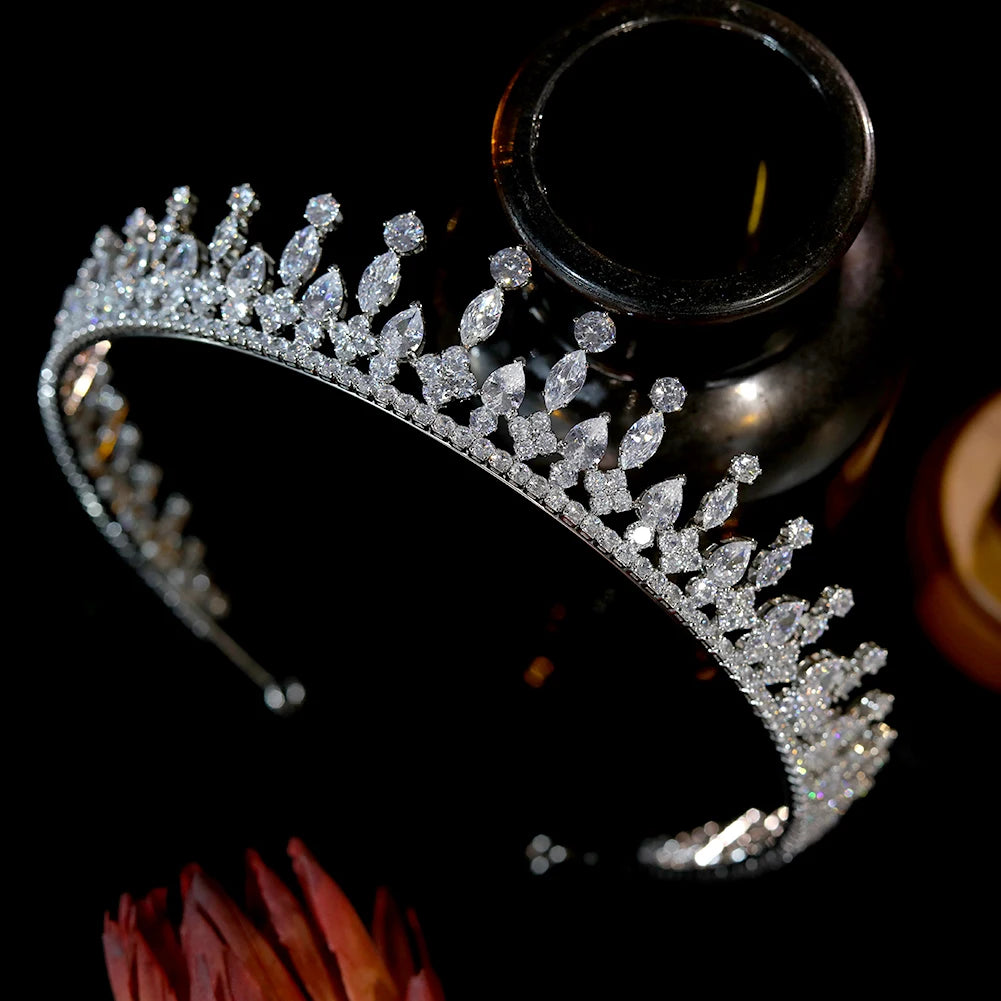 Glamorous silver rhinestone graduation crown and wedding tiara displayed on a dark luxury glass vase.