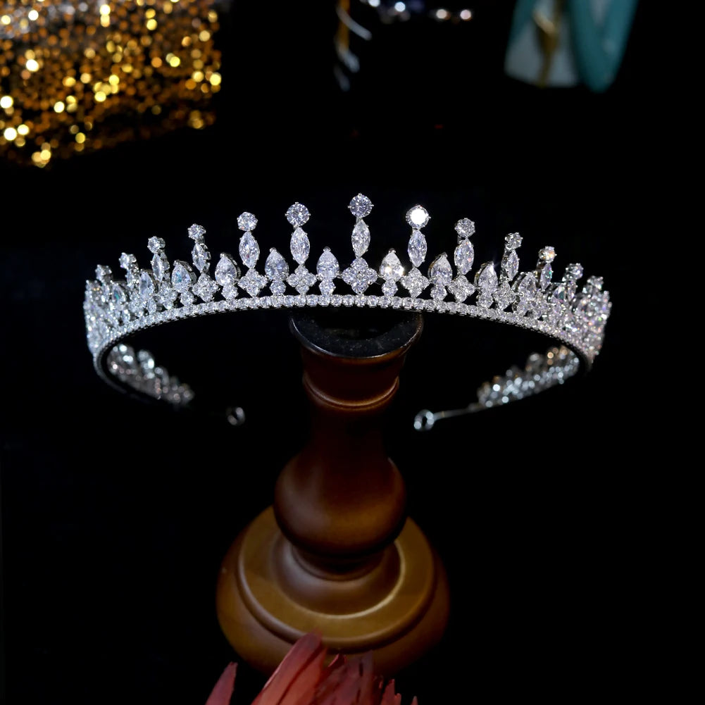 Front profile view of an elegant crystal bridal crown meticulously balanced on a wooden display pedestal.