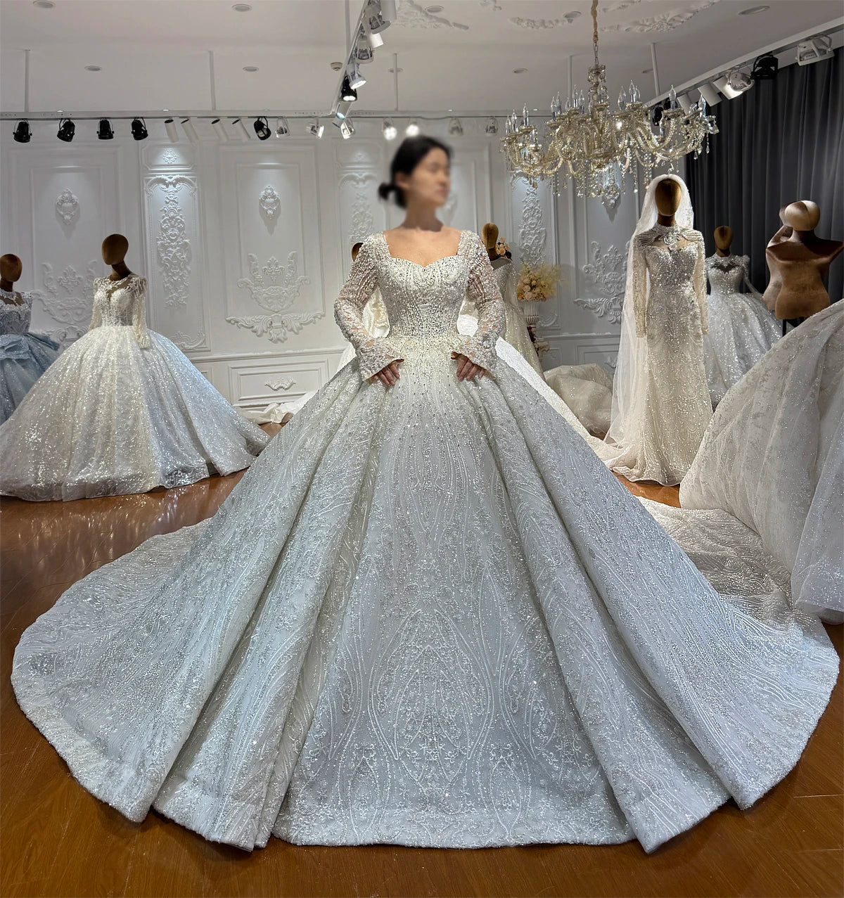 Front perspective of a model showcasing the heavy crystal embroidery and grand flared skirt of an elegant full beaded lace wedding gown with long sleeves.