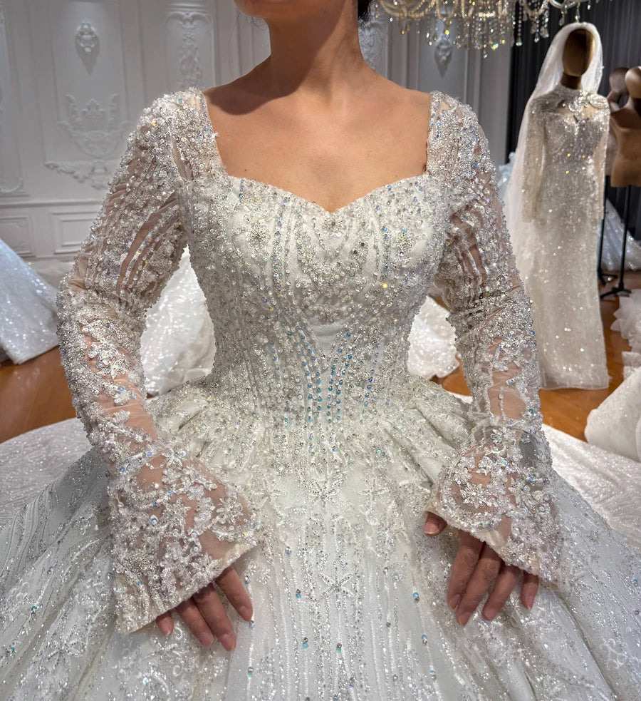 Close-up of a model wearing an elegant full beaded lace wedding dress, highlighting the sweetheart neckline, heavily embellished bodice, and graceful trumpet sleeves.