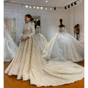 Front perspective of an elegant Muslim bridal gown in a boutique, featuring modest long sleeves, a high neck, full crystal beading, and a sweeping, textured ball gown train.