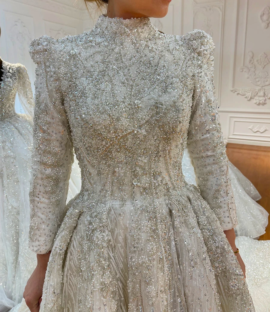 Close-up detail of the bodice on a luxury modest wedding dress, showcasing intricate full beading, a high neckline, and slightly puffed shoulders for a royal bridal look.