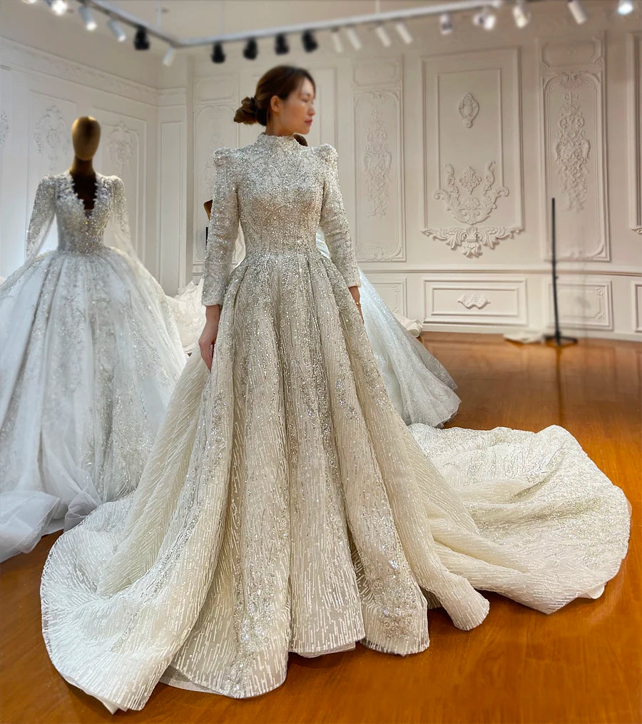 Full-length front view of a model wearing an elegant full-beaded Muslim bridal gown, highlighting the modest long-sleeve design and a grand, heavy cathedral-length train.