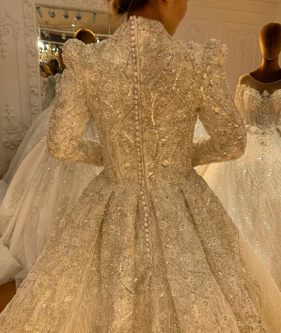 Close-up back view of a modest long-sleeve bridal gown, featuring an elegant row of pearl buttons down the back and heavy, shimmering crystal beadwork.