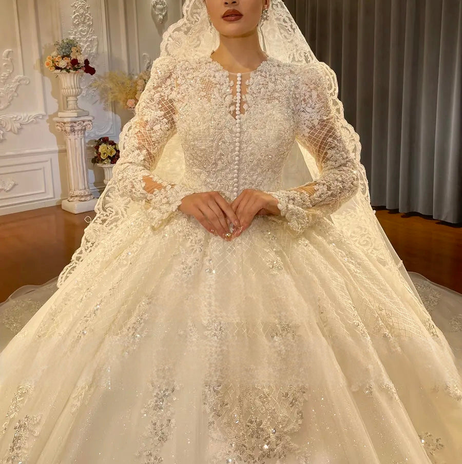 Close-up detail of the bodice on a timeless full lace ball gown wedding dress, highlighting the delicate lace appliqués, high illusion neckline, and long sleeves with pearl buttons.