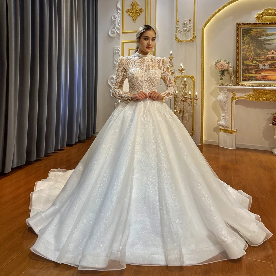 Full front view of a model wearing an elegant fully beaded illusion A-line wedding dress featuring a high neck, long sleeves, and a voluminous sparkly skirt.