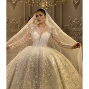 Close-up of an elegant lace appliqué ball gown wedding dress featuring a shimmering beaded bodice, illusion long sleeves, and a matching long bridal veil.