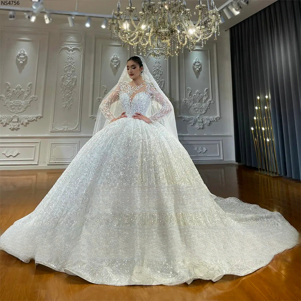 Stunning long sleeve wedding dress with a voluminous sparkly skirt and floral lace appliqué, captured in a full-length pose for high-end bridal inspiration.