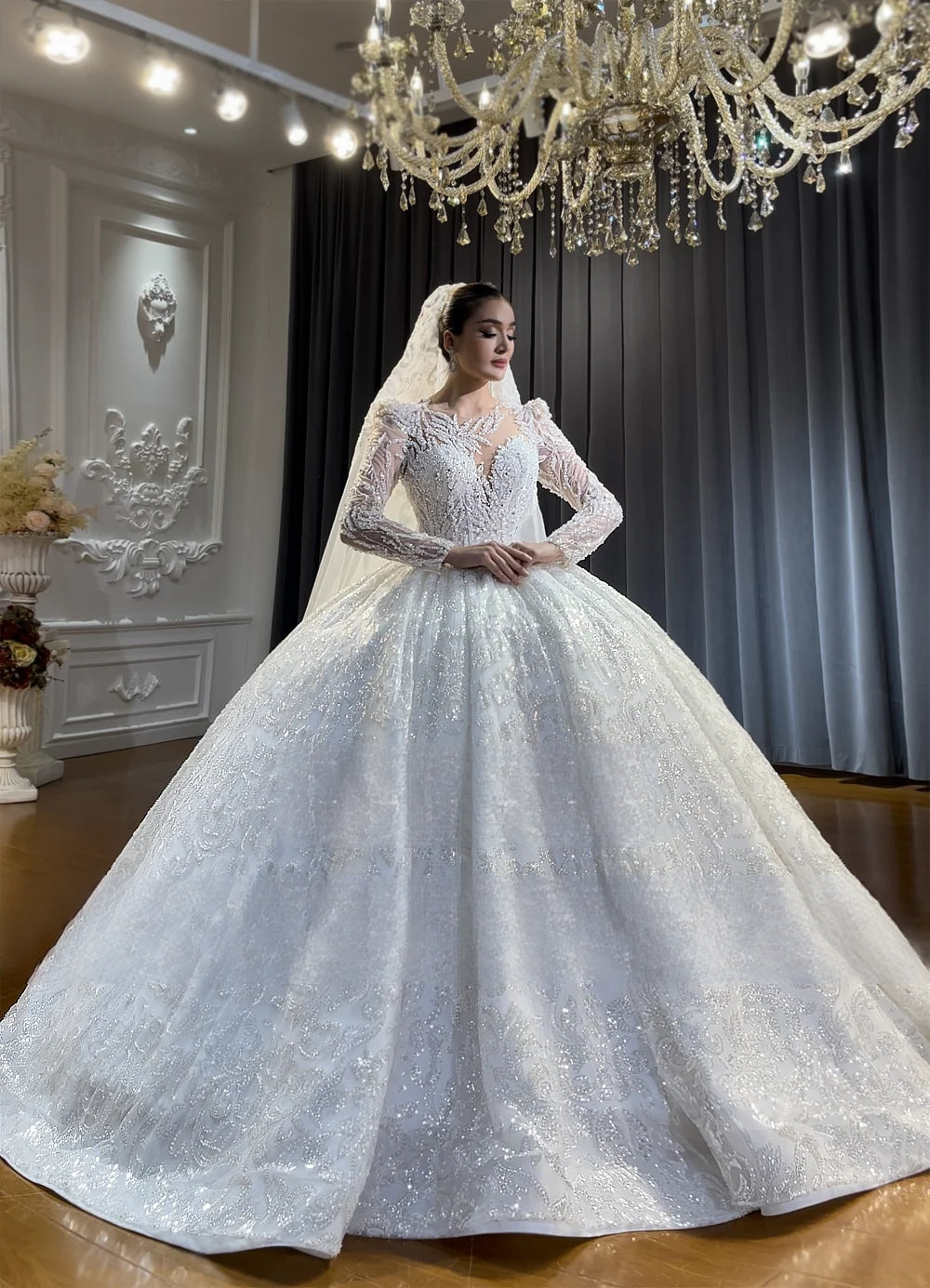 Front perspective of a regal lace appliqué ball gown wedding dress with illusion sleeves, highlighting the heavy crystal embellishments and massive shimmering skirt.