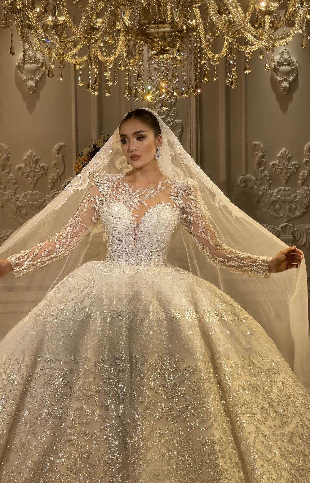 Detailed view of a beaded bridal gown bodice with delicate leaf-patterned lace appliques and a shimmering neckline, reflecting light from a luxury crystal chandelier.
