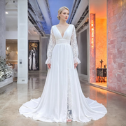 Elegant bride modeling a white lace and chiffon beach wedding dress with a deep V-neckline, long sheer floral sleeves, and a high leg slit.