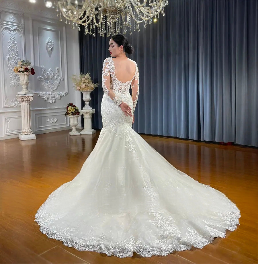 Back view of a stunning fit and flare wedding dress highlighting the low open back, long lace sleeves, and a voluminous cathedral-length lace train extending across a wood floor.