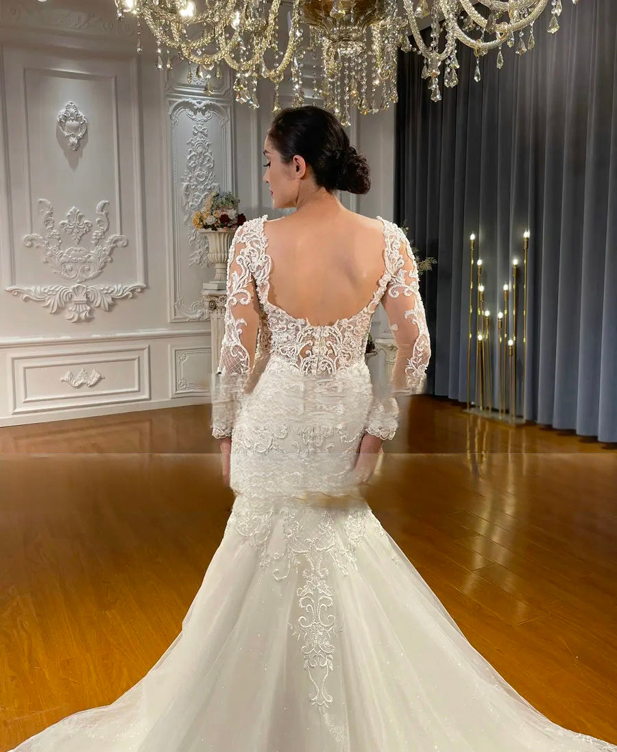 Detailed view of the sheer lace back and intricate embroidery of an elegant mermaid wedding gown, featuring a low-scoop back design and delicate long sleeves.