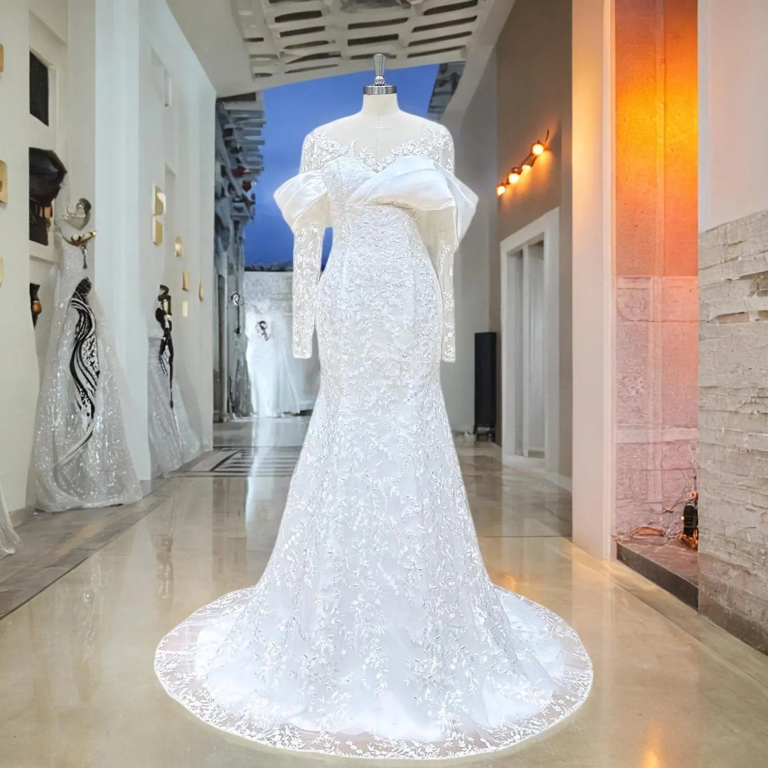 Mannequin display of an elegant white lace mermaid wedding dress highlighting the long sheer sleeves, illusion O-neck, and a unique folded satin bust detail in a bridal boutique.