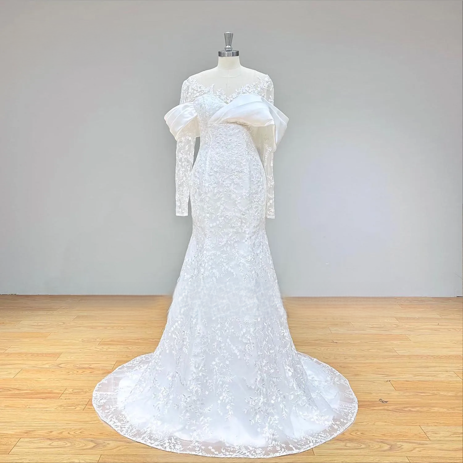 Studio shot of an elegant long sleeve lace mermaid wedding dress on a mannequin, showing the full front silhouette, illusion O-neckline, and sparkling floral lace appliqués.