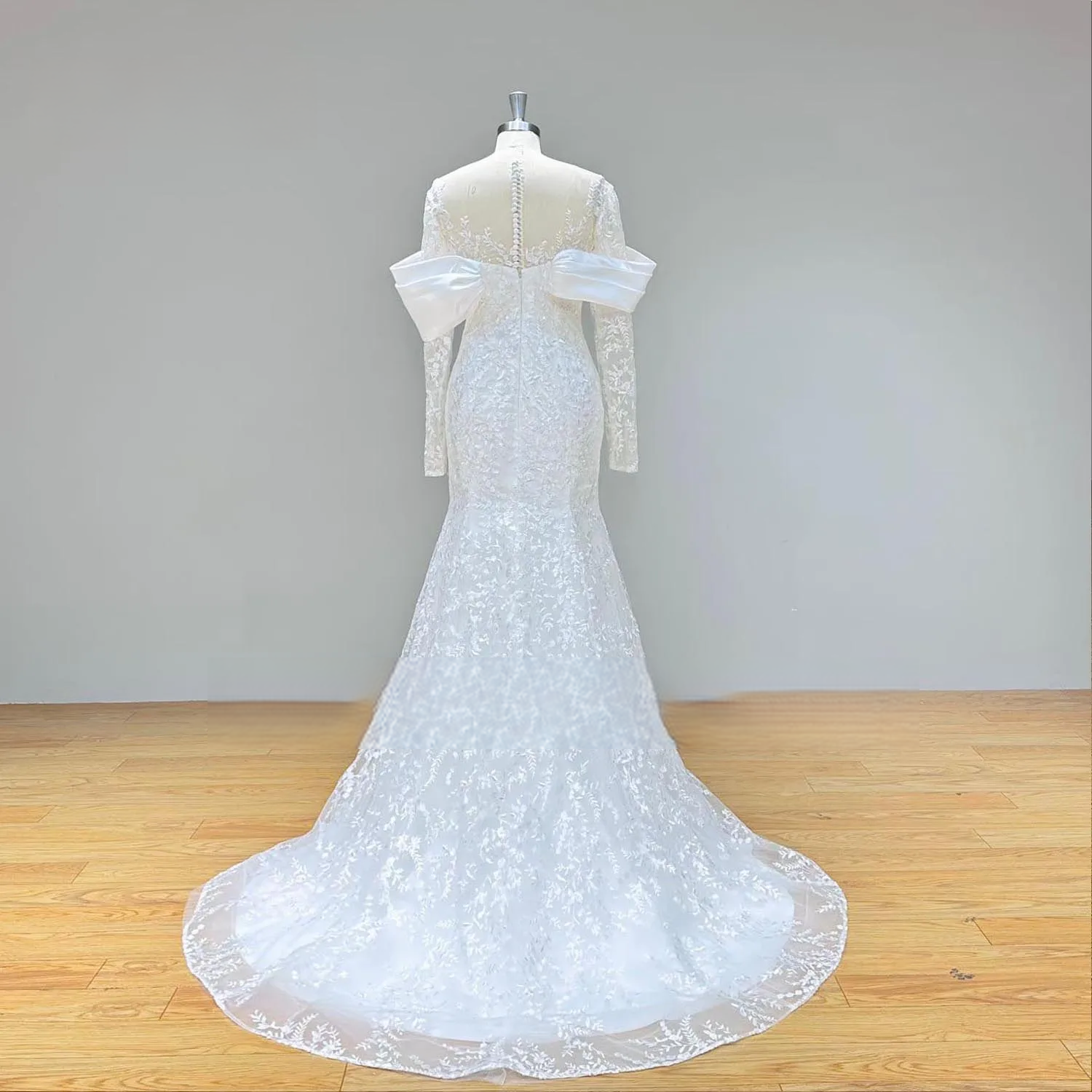Back view of an elegant lace mermaid wedding dress on a mannequin, emphasizing the sheer illusion back, row of delicate buttons, and trailing chapel train.