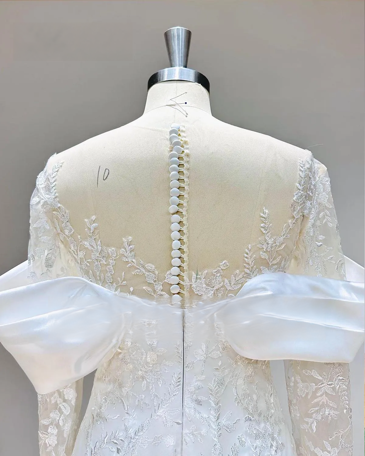 Close-up of the elegant illusion back on a long-sleeved lace mermaid wedding dress, featuring a traditional line of pearl buttons and striking satin back bows.