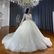 Front view of an elegant lace wedding dress with a square neckline, long sleeves, and a shimmering ball gown skirt.