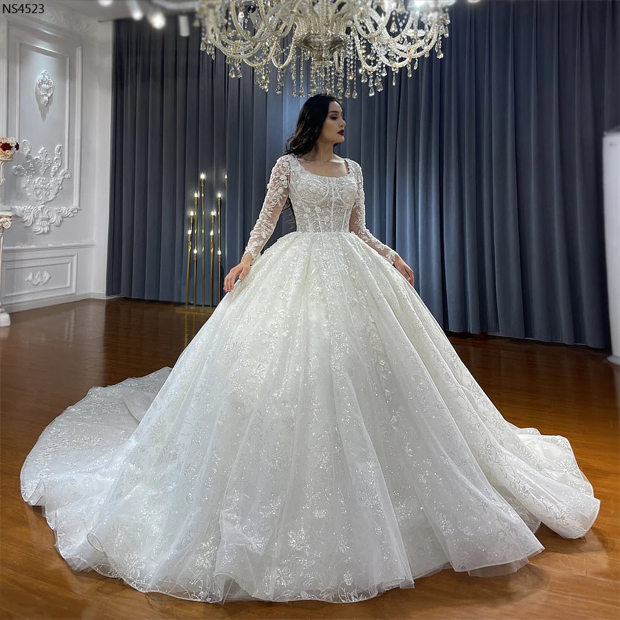 Front view of an elegant lace wedding dress with a square neckline, long sleeves, and a shimmering ball gown skirt.