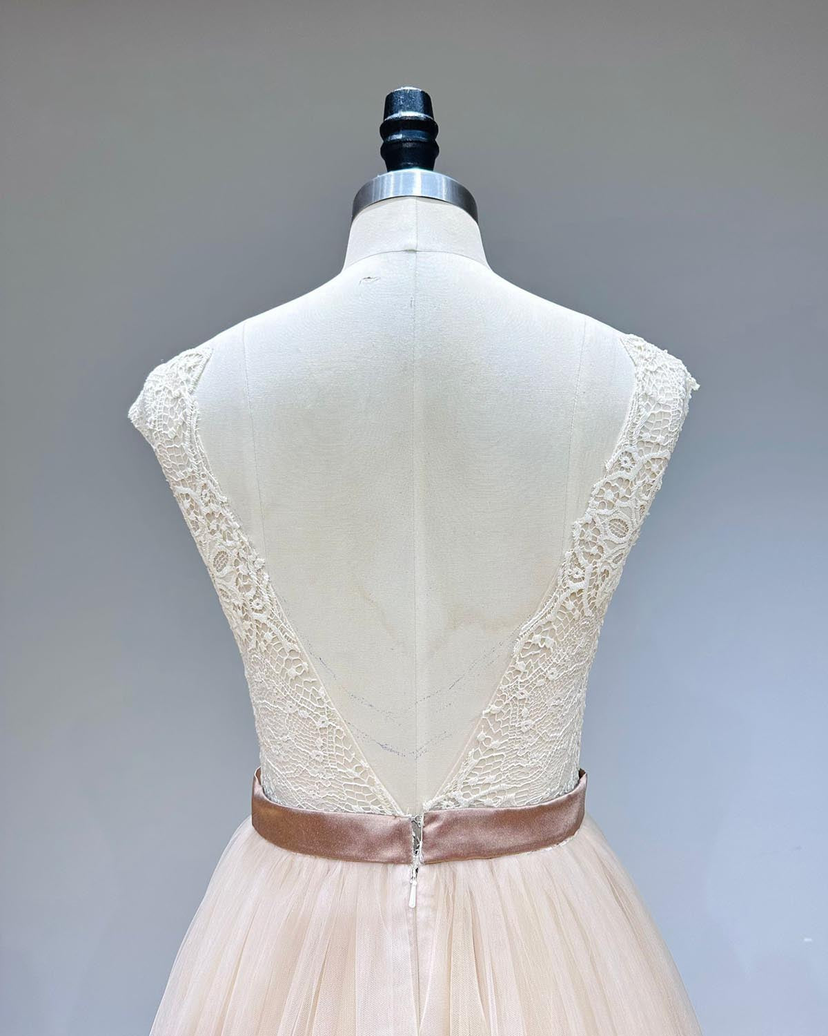 Back view detail showcasing the elegant V-backless lace design and waist ribbon on a layered tulle evening dress.