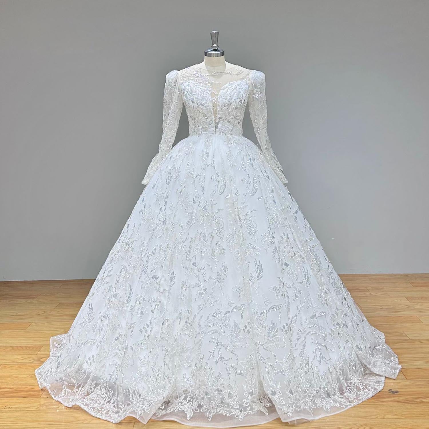 Full front view of an elegant long-sleeve ball gown wedding dress with a full tulle skirt displayed on a showroom mannequin.