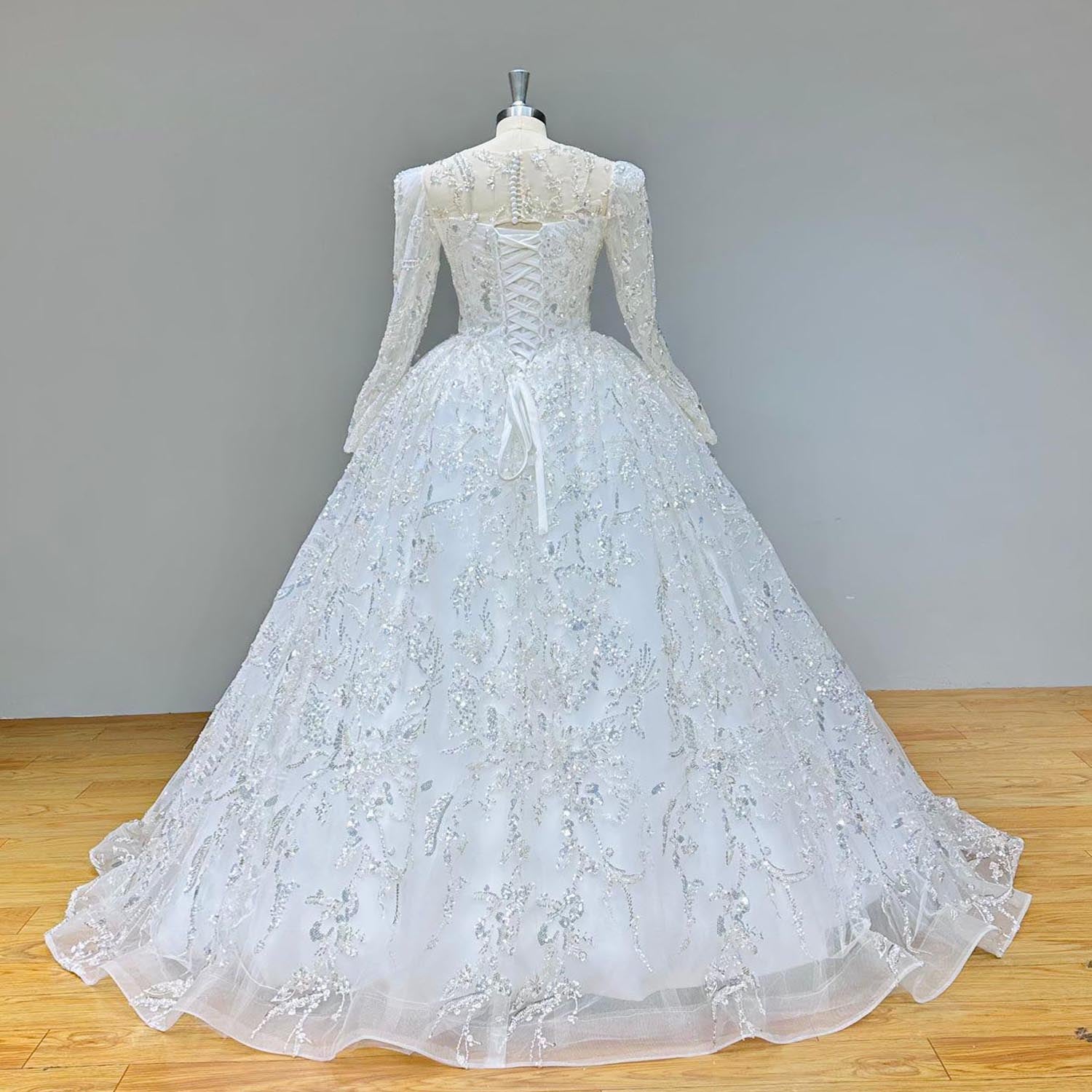 Full back view of a long-sleeve ball gown wedding dress with a detailed illusion back and lace train displayed on a mannequin.