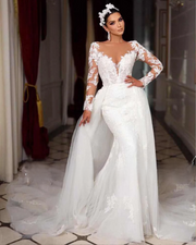 Elegant bride modeling a long sleeve mermaid wedding dress featuring exquisite lace appliques, an illusion neckline, and a voluminous detachable train in a luxury setting.