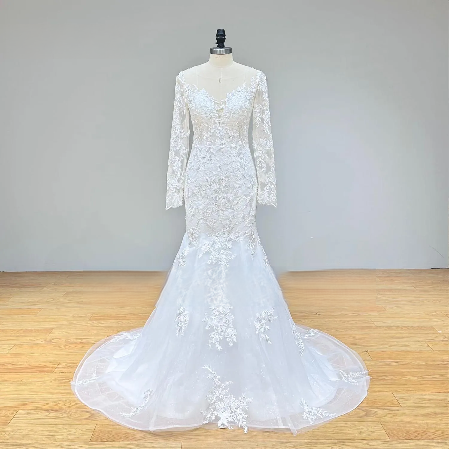 Front view of a long sleeve mermaid wedding dress with its detachable train removed, emphasizing the fitted, lace-appliqued silhouette and flared hem.