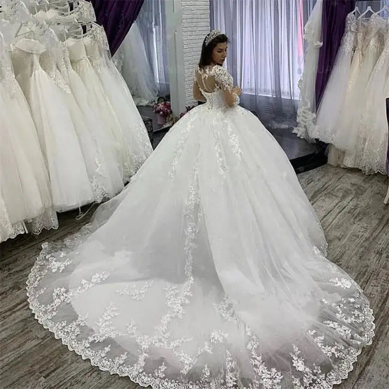 Detailed back view of the long sleeve plus size bridal gown, showcasing a romantic low lace-up corset back design, sheer illusion lace accents, and a sweeping chapel-length train.