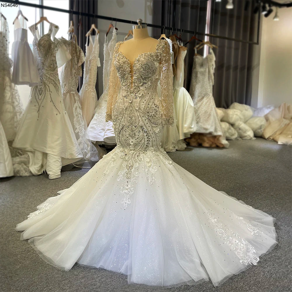 Luxury mermaid bridal gown on a mannequin, highlighting the shimmering silver lace embroidery and long sheer beaded sleeves in a bridal showroom.