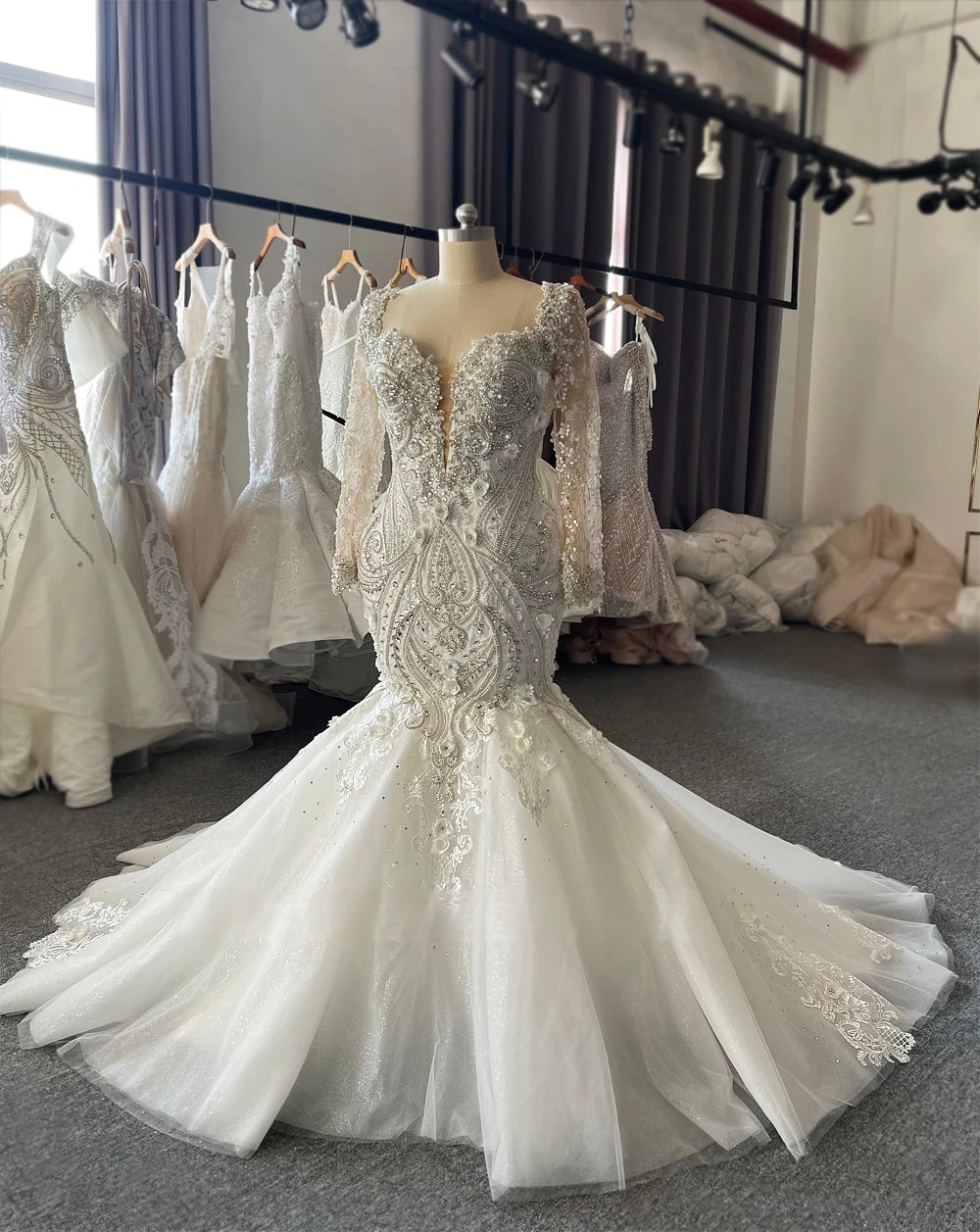 Front-side angle of the lace mermaid wedding gown on a mannequin, emphasizing the fitted silhouette and the spread of the sparkling chapel-length train.