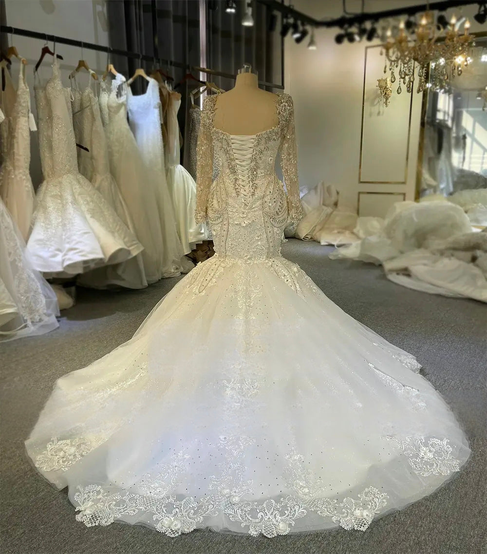 Rear view of the mermaid bridal gown on a mannequin, displaying a traditional lace-up corset back and a wide, lace-trimmed circular train.