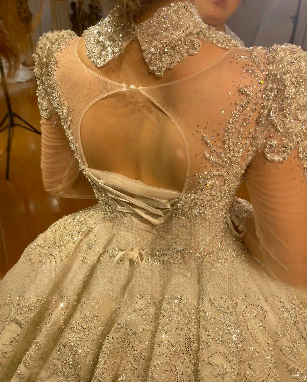 Close-up of the back of a luxury wedding gown featuring an illusion keyhole back, high beaded collar, and intricate corset lacing detail.