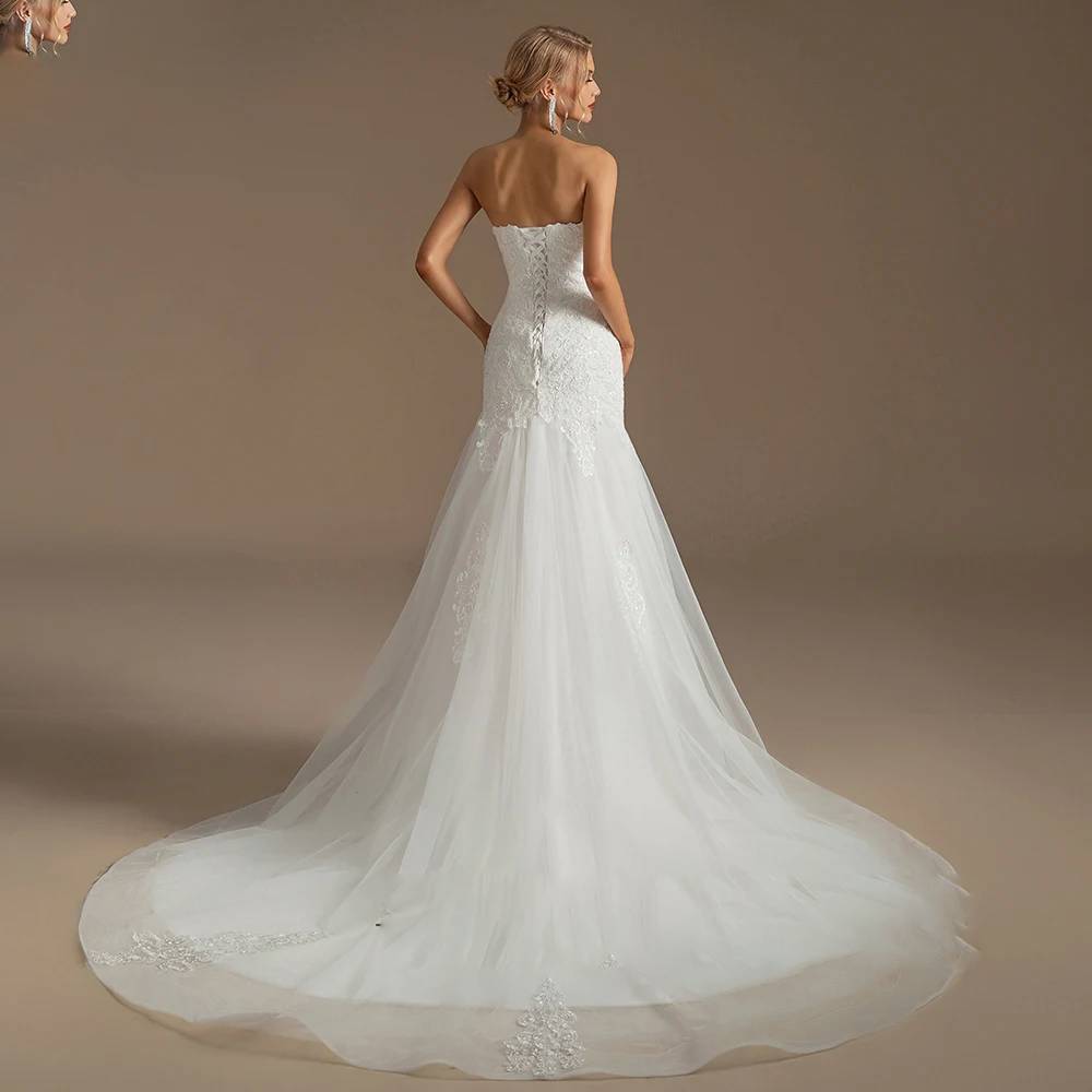 Back view of a strapless mermaid bridal dress highlighting a romantic lace-up corset back and a dramatic tulle train with lace appliqué trim.