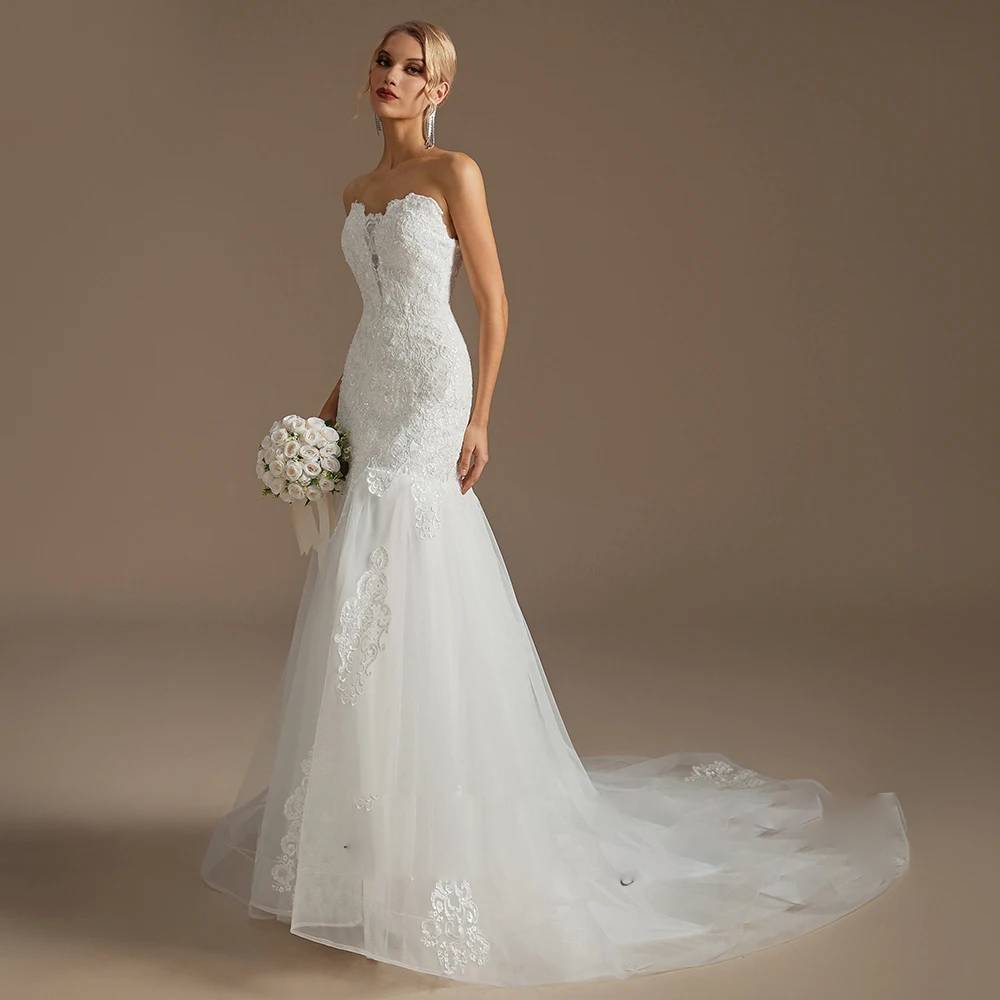 Three-quarter profile of a model holding a white rose bouquet in a strapless lace mermaid wedding gown with an extended chapel train.