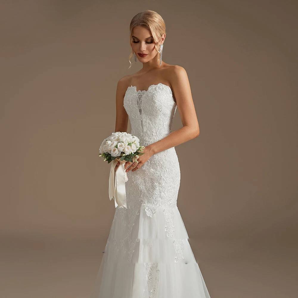 Mid-shot of a bride holding a rose bouquet, showcasing the intricate floral lace details and sweetheart neckline of the mermaid dress.