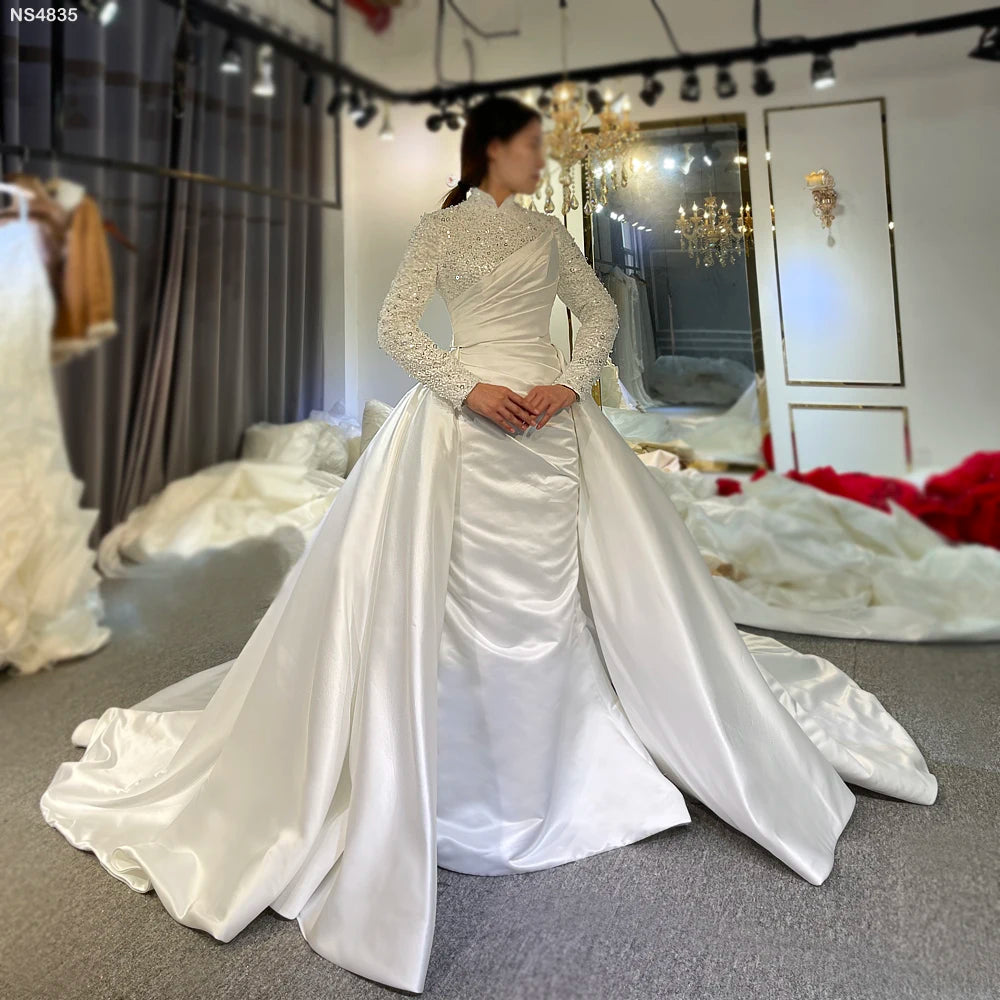 Front view of an elegant Muslim satin wedding dress featuring modest long beaded sleeves, a high neck, and a versatile 2-in-1 design with a detachable grand satin overskirt.