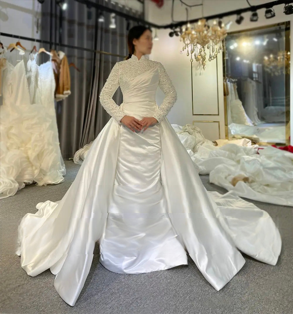 Modest bridal gown with shimmering long sequined sleeves and a high neck, showcasing the sophisticated 2-in-1 skirt design and draped satin bodice detail.
