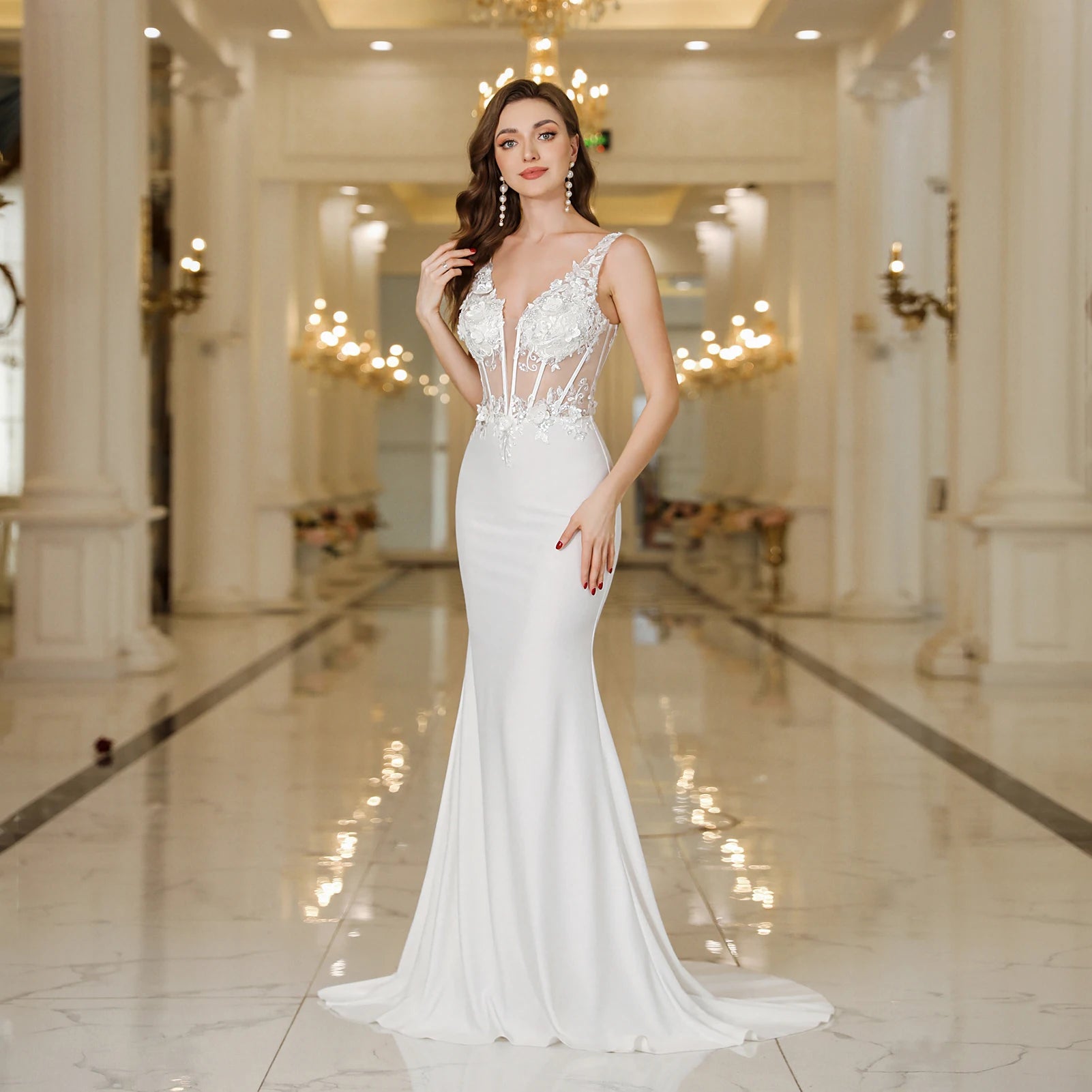 Professional model posing in a white mermaid-style evening dress featuring a sheer bodice with white beaded appliques and a sleek floor-length skirt in a luxury hall.